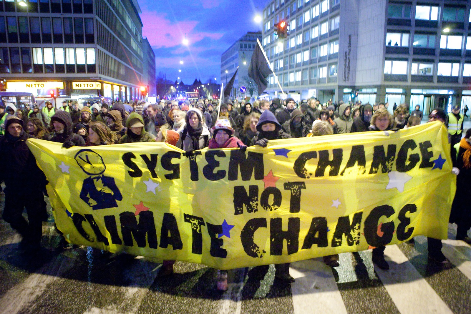Group of people rallying in street carrying yellow sign that says System Change Not Climate Change. photo credit: kris krüg